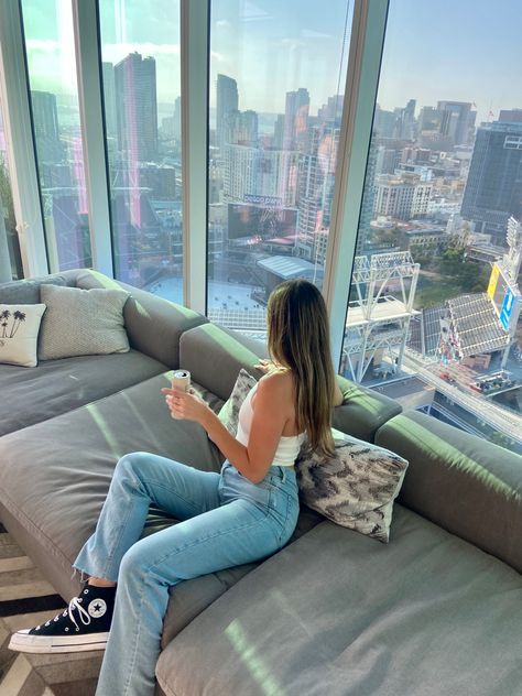 Female sitting on a couch looking out the window over downtown San Diego near Padres stadium San Diego Aesthetic Pictures, San Diego Lifestyle, San Diego College Aesthetic, Sdsu Aesthetic, San Diego High Rise Apartment, Aesthetic San Diego, San Diego Apartments, High Rise Apartment, Luxury High Rise