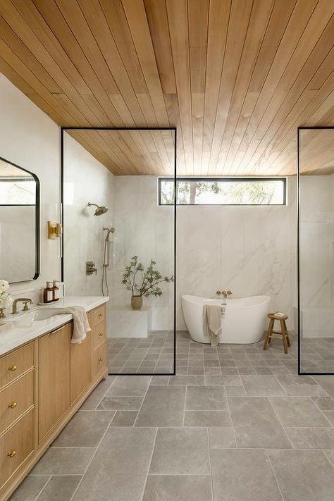 Spacious bathroom features an oval bathtub inside a walk in shower with his and hers shower benches, a clerestory window, a satin nickel shower kit on marble slab shower walls, gray grid shower floor tiles, a steel partition, a brown reeded double washstand with marble countertop with brass faucets under curved black mirrors lit by brass and glass sconces and a teak plank ceiling. Lhk Interiors, Bathroom Renovation Cost, Bad Inspiration, Trendy Bathroom, Bathroom Pictures, Grey Bathrooms, Wet Rooms, Shower Design, Modern Bathroom Design