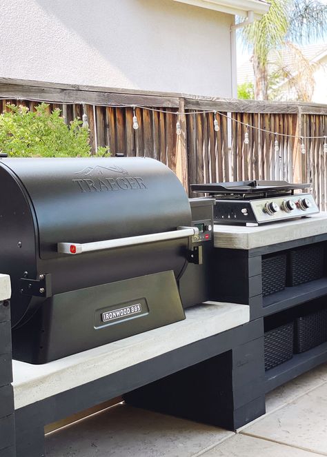 Black Traeger Grill and a stove top placed on a black and white custom countertop Traeger Grill Outdoor Kitchen, Outdoor Kitchen For Traeger Grills, Back Patio Grill Ideas, Blackstone And Smoker Outdoor Kitchen, Black Stone Grill Station, Diy Outdoor Traeger Grill Station, Outdoor Kitchen With Traeger Grill And Blackstone, Outdoor Corner Grill Area, Outdoor Kitchen Traeger Grill