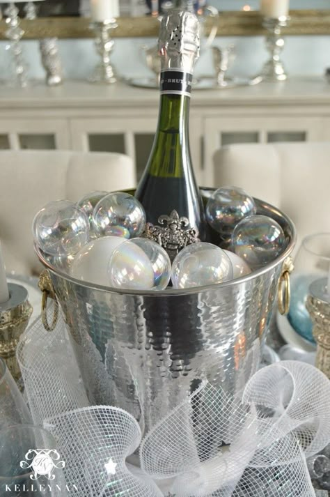 Blue and Silver New Year's Eve Table Ideas- Ball Ornament Champagne Blubbles- Champagne bucket centerpiece and lantern party hats Champagne Bottle Centerpiece Ideas, Champagne Bucket Centerpiece, Champagne Centerpiece Ideas, New Years Centerpieces, Champagne Centerpieces, New Year Centerpiece Ideas, Bucket Centerpiece Ideas, Champagne Bucket Decor, Champagne Centerpiece