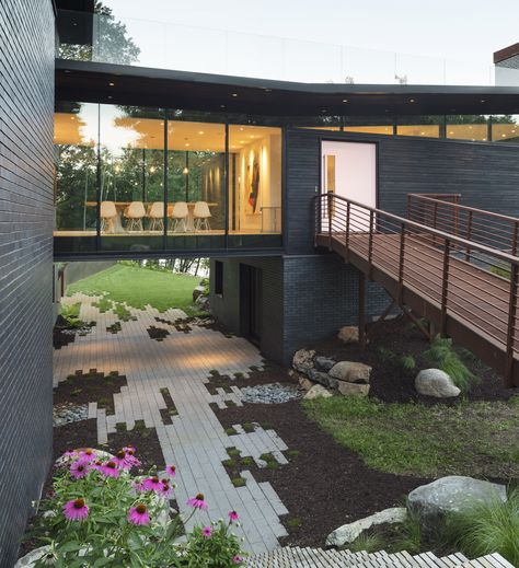 This sculptural home set deeply into the hillside of the Stillwater countryside features charred wood siding (shou sugi ban), cantilevered roof overhangs, and a glass bridge that visually separates the public and private spaces of the house. House Bridge Walkways, Bridge Entrance To House, Glass Atrium House, Bridge To House Entrance, Bridge In House, Houses With Bridges, House With Bridge, Bridge Homes, Cantilever Roof