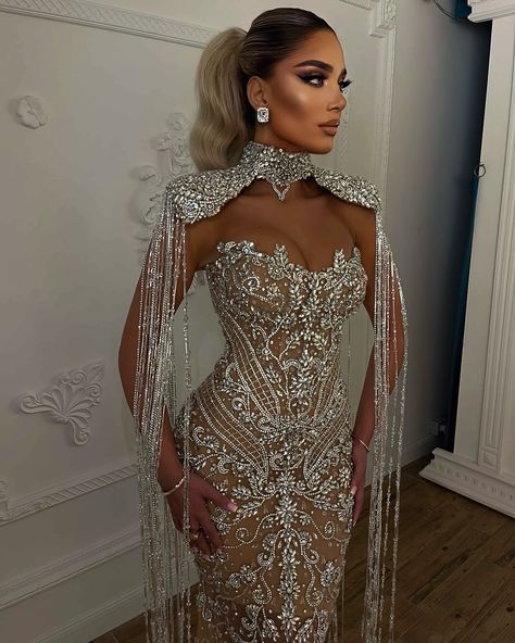 To order this gown, send us a DM at @reineecouture. This couture gown is a masterpiece of opulence and intricate design, perfect for making a grand entrance at any high-profile event. The gown features a form-fitting silhouette that gracefully accentuates the body’s natural curves, exuding both elegance and sophistication. **Bodice and Neckline:** - The bodice showcases a dramatic sweetheart neckline, intricately adorned with shimmering crystals and pearls. - An exquisite high-neck collar a... Nude Gown, Custom Made Dresses, Champagne Evening Dress, Silver Gown, Shoulder Cape, Formal Occasion Dress, Exquisite Gowns, Embellished Gown, Stunning Gowns