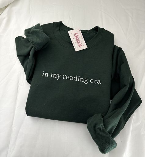 Step into your reading era with our "In My Reading Era" embroidered sweatshirt, a must-have for every book lover. This minimalist book sweatshirt, a perfect book club gift, effortlessly combines comfort and literary style, ensuring you join the exclusive ranks of the Reading Crew with unparalleled flair. Color in example is  Forest Green * 50% cotton, 50% polyester * Pre-shrunk * Classic fit * 1x1 athletic rib knit collar with spandex * Air-jet spun yarn with a soft feel and reduced pilling * Do Minimalist Book, Bookclub Gifts, Lover Sweatshirt, Book Clothes, Embroidered Sweatshirt, Embroidered Sweatshirts, New Wardrobe, Book Lover, Graphic Shirts