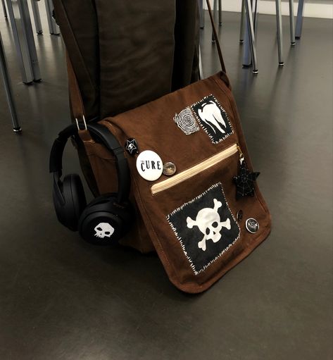 A brown bag with lots of black and white selfmade accessories Alt Schoolbag, Cross Body Bags Aesthetic, Bag Patches Aesthetic, Goth Backpack Diy, Diy Fabric Accessories, Cute Cross Body Bags, Pin Bags Ideas, Diy Fabric Bag, Punk Bag Diy