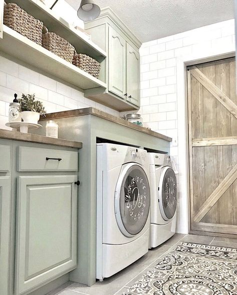 Light green floating shelves and cabinets with black pulls and knobs are mounted on white laundry room wall tile. An enclosed white front load washer and dryer set are topped with a butcher block countertop. Subway Tile Laundry Room, Elegant Laundry Room, Farmhouse Laundry Room Ideas, Grey Laundry Rooms, Room Wall Tiles, White Laundry Rooms, Green Laundry, Basement Laundry Room, White Laundry