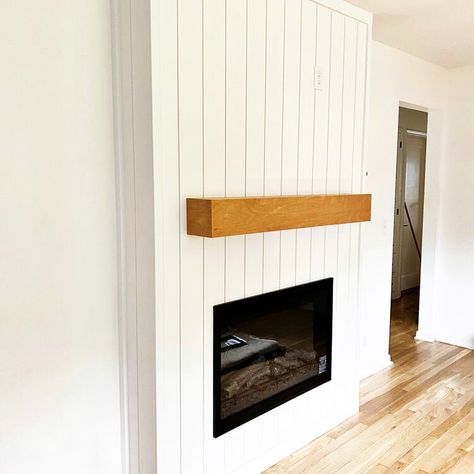 Fireplace surround in Lincoln, NE, featuring vertical shiplap painted white, black electric fireplace, and custom wood mantle in honey-colored stain. Vertical Shiplap Mantle, Shiplap On Sides Of Fireplace, Shiplap Vertical Fireplace, White Wood Panel Fireplace Wall, Vertical Panel Fireplace, Diy Vertical Shiplap Fireplace, Vertical Paneling Fireplace, Vertical Boards On Fireplace, Vertical Shiplap On Fireplace