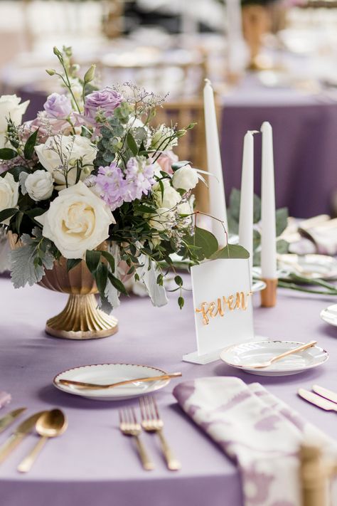 Table Place Setting Decor with Lavender Linens, Gold Silverware, White Taper Candles, and White and Purple Floral Centerpiece Arrangement Light Purple Wedding Centerpieces, Ivory And Purple Wedding, Lilac And White Decorations, Violet Wedding Decorations, Simple Purple Wedding, Blush Pink And Lavender Wedding, Lavender Reception Decorations, Purple And Gold Table Decor, Wedding Centerpieces Lavender