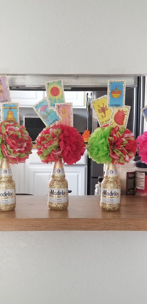 Beautiful Modelo glitter bottle with 3 tissue Mexican flowers and loteria cards. Taco Party Centerpiece Ideas, Centerpiece For Fiesta Party, Modelo Bottle Centerpieces, Mexican Themed Party Centerpieces, Three Esta Centerpieces, Mexican Theme Graduation Party Centerpieces, Mexican Theme Table Centerpieces, Fiesta Theme Table Centerpieces, Bottle Centerpieces Birthday