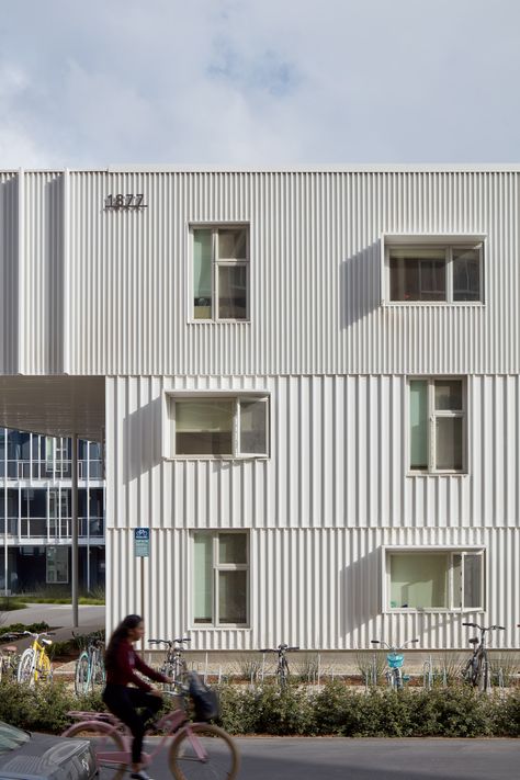 LOHA's San Joaquin Student Housing For the perimeter elevations, the team used white, corrugated metal cladding that evokes shipping containers. The courtyard-facing walls are sheathed in grey plaster.  White-painted steel was used for the outdoor staircases and corridors. Aluminium fins frame the corridors, helping reduce sun exposure. Multifamily Architecture, Metal Facade, Passive Design, Metal Cladding, Creative Architecture, Student Housing, Student House, White Building, Corrugated Metal