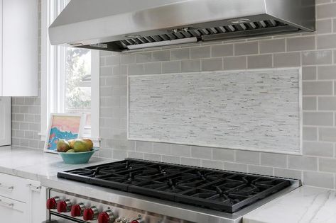 White mosaic cooktop backsplash tiles keep a classic neutral finish surrounding light gray subway tiles under a stainless steel vent hood. Gray Subway Tiles, Cooktop Backsplash, Gray Kitchen Design, White And Gray Kitchen, Stainless Steel Hood Vent, Subway Tile Design, Grey Subway Tiles, Steel Hood, Grey Kitchen Designs