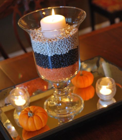 Halloween Centerpiece  check it out at www.partylite.biz/HeavenlyAdriana..... Ward halloween party centerpiece- green placemat, small drinking glasses, tealights, pumpkins/ gourds from outside, green lentils, black beans, corn kernels, red beans, white beans Halloween Glass Vase Filler Ideas, Candy Corn Vase Centerpieces, Adult Halloween Party Decorations, Candy Corn Apothecary Jars, Glass Hurrican Centerpieces Fall, Dekorasi Halloween, Diy Halloween Decor, Halloween Centerpiece, Adult Halloween Party