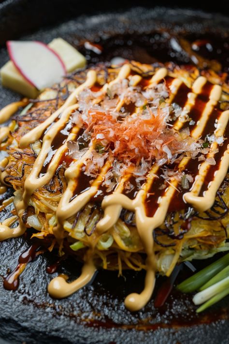 Okonomiyaki topped with drizzles of mayonnaise, a savory sauce, and bonito flakes on a dark plate, garnished with sliced radish. Japanese Okonomiyaki Recipe, Japanese Pancake Okonomiyaki, Traditional Japanese Dinner, Traditional Japanese Food Recipes, Yaki Imo, Japanese Okonomiyaki, Eggplant Rollatini Recipe, Okonomiyaki Recipe, Quiche Lorraine Recipe