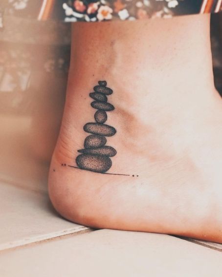 15 Beautiful Ankle Tattoos and Their Meanings You May Love to Try! Zen Tattoos For Women, Mens Ankle Tattoos Ideas, Tat Cover Up Ideas, Ebenezer Stone Tattoo, Rock Tattoo Ideas Stones, Rock Cairn Tattoo, Petoskey Stone Tattoo, Cover Up Tattoo Ankle, Outside Ankle Tattoo