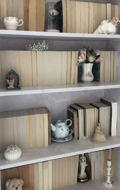 coquette white bookcase with antiques / china and flowers  on it Coquette Bookshelf Aesthetic, Coquette Book Shelf, Coquette Shelves, Coquette Shelf Decor, Vintage Book Shelf Aesthetic, Octavia Aesthetic, White Bookshelf Aesthetic, Coquette Library, Coquette Shelf