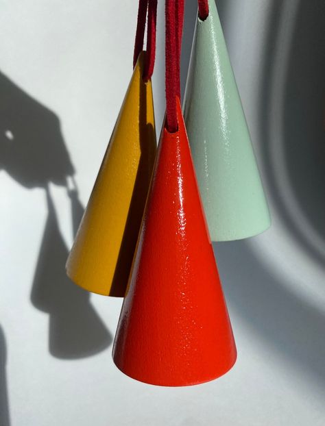 A set of three wooden, cone shaped hand painted Christmas tree ornaments in colors of mustard yellow, bright red, and eggshell blue are pictured with a white background. These three Christmas ornaments are held up by vegan red leather cords strung through the tops of each ornament. A shadow of the hand holding the ornaments is seen in the background. Colorful Minimalism, Modern Christmas Ornaments, Eggshell Blue, Cone Trees, Modern Christmas Tree, Wood Christmas Ornaments, Wood Christmas, Wooden Plates, Hand Painted Ornaments