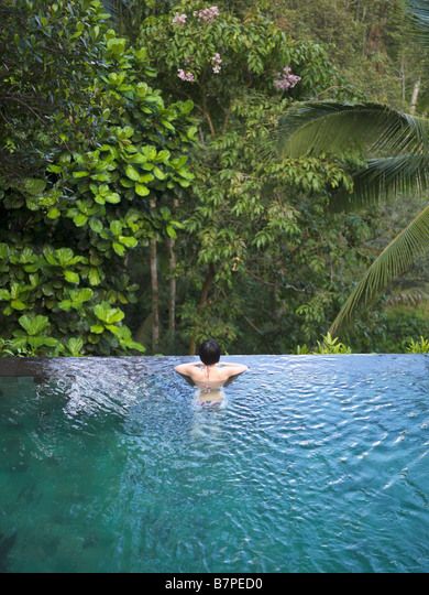 Woman bathing in an infinity pool surrounded by a lush tropical forest. Stock Photo Infinity Pool Tropical, Pool In Forest, Infinity Pool Backyard, Luxury Poolside, Tropical Colonial, Rent House, Indoor Waterfall, Pool Waterfall, Fantasy Life