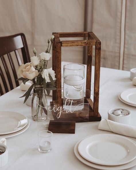 wedding guest table decor ideas rustic simple DIY hand made wooden lanterns with floating candle in vase milk jar with bud flowers centerpiece acrylic see through table numbers with wood base simple center piece decor ideas Floating Candle Lanterns, Floating Candles On Wood Centerpieces, Rustic Elegant Wedding Table Settings, Wood Lantern Table Centerpieces, Rustic Floating Candle Centerpieces, Diy Wood Lanterns Wedding, Wood Frame Centerpiece Wedding, Wooden Lantern Wedding Centerpieces, Wood Lanterns Wedding Centerpiece Ideas