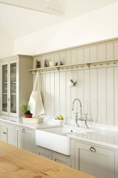 Stunning grey colored kitchen with custom shaker cabinets adorned with cup pull hardware alongside a dual farmhouse sink with bridge faucet framed by white stone counters which pair with a gray tongue and groove backsplash accented with cup hook shelf beside a countertop glass front hutch. Beadboard Kitchen Backsplash, Kitchen Devol, Beadboard Kitchen, Devol Kitchens, Beadboard Backsplash, Kitchen Farmhouse, Shaker Kitchen, Chic Kitchen, Cottage Kitchen