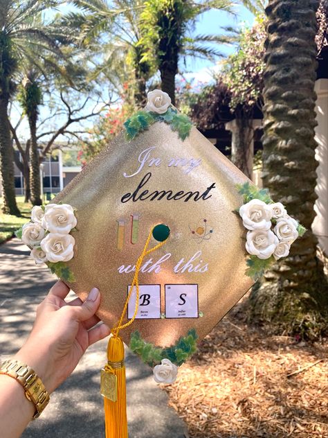 Chemistry themed graduation cap decoration. 
Gold background with white and black letters reading “In my element with this B.S”  
Element used for the B.S (bachelor of science) B for Boron and S for Sulfur. 
Green leaves and white roses on each corner. Cap Decoration Graduation Biology, Science Major Graduation Cap, Graduation Cap Designs College Biology, Forensic Chemistry Graduation Cap, Chemistry Graduation Cap Ideas, Chemistry Cap Decoration, Chemical Engineering Graduation Cap, Physics Graduation Cap, Biology Grad Party