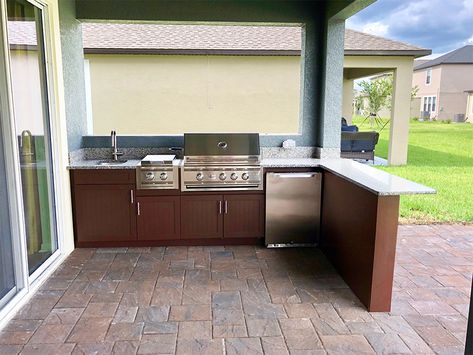 This amazing L-shaped kitchen island features a Summerset Grill, side burner, beverage refrigerator, sink, granite countertops and brown custom Starboard cabinetry. The bar height and expanded design creates a comfortable place for friends and family to gather while you grill. Straight Outdoor Kitchen, L Shaped Outdoor Kitchen With Bar, L Shape Outdoor Kitchen, L Shaped Outdoor Kitchen, Kitchen L Shaped, Kitchen Bar Height, Covered Lanai, Outdoor Living Kitchen, L Shaped Bar