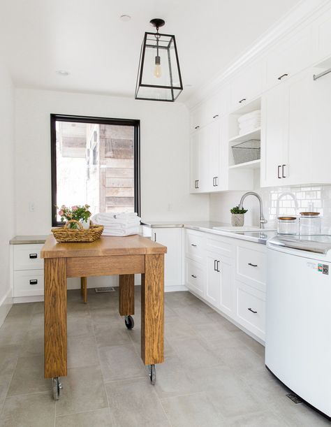 This laundry room comes with a wood island on casters, making it easy to move the large piece around if need be. Laundry Room Island, Perfect Laundry Room, White Laundry Rooms, Dark Countertops, Beadboard Backsplash, White Laundry, White Shaker Cabinets, Modern Mountain Home, Stainless Steel Countertops