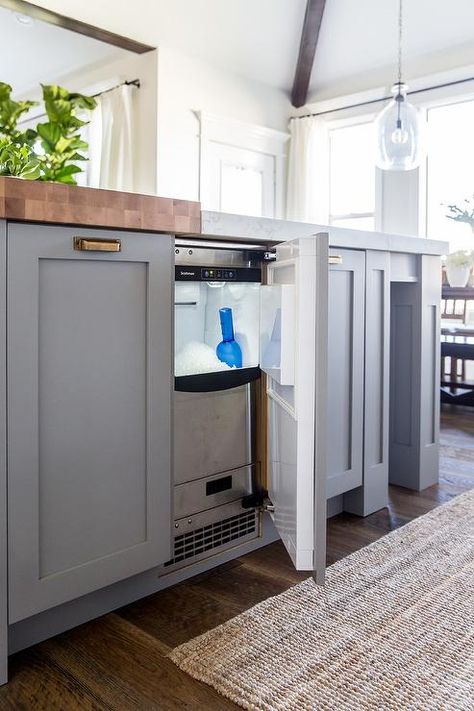 A stainless steel ice maker is concealed behind a cabinet door of a gray blue kitchen island accented with antique brass cup pulls and butcher block top and white quartz countertop. Built In Icemaker In Kitchen, Icemaker In Kitchen Island, Undercounter Ice Maker, Sink Dishwasher, Grey Blue Kitchen, Freezer Drawer, Blue Kitchen Island, Drink Fridge, Grey Kitchen Island