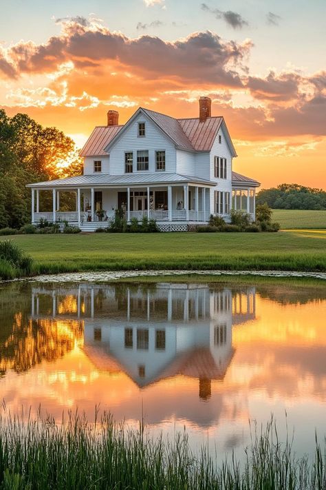 White farmhouse with large wraparound porch large pond with reflection of the house in front sunset scene scenic farmland landscape. The whimsical allure of countryside houses makes these charming abodes more than just a roof and four walls amidst the rolling hills and chattering wildlife. Farmhouse With Land, White Country House, Future House Exterior, Farmland Landscape, Large Pond, Backyard Flowers Garden, Wraparound Porch, Farmhouse Architecture, Porch Columns