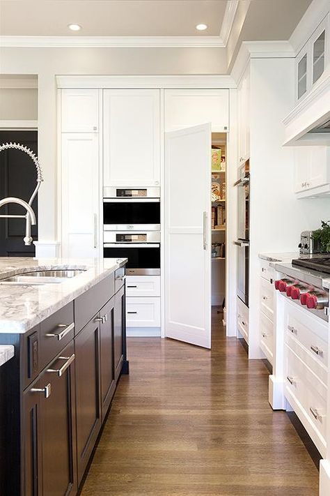 A hidden pantry door is positioned beside stacked microwaves fixed above and below white shaker cabinets in this well appointed kitchen featuring a chocolate brown island accented with nickel hardware and a gray quartzite countertop finished with a stainless steel dual sink with a stainless steel pull out faucet. Hidden Pantry Door, Pantry Door Decor, Organizing Kitchen Countertops, Kitchen Liners, Chocolate Kitchen, Modern Pantry, Replacing Kitchen Countertops, Brown Kitchen Cabinets, Hidden Pantry