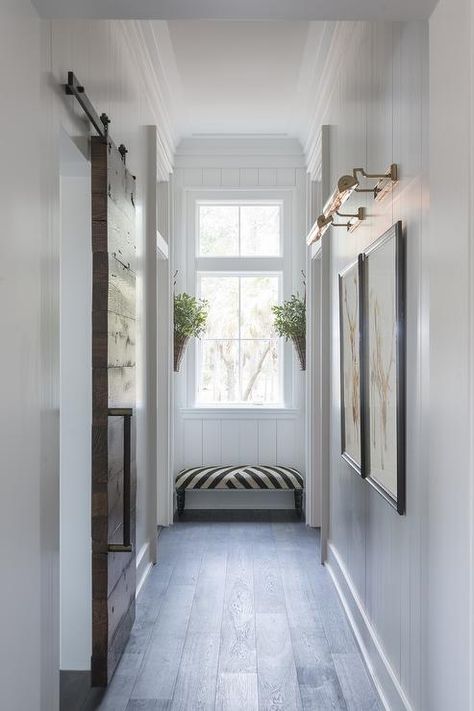 Chic hallway features vertical shiplap walls lined with side by side art illuminated by antique brass picture lights situated across from a plank barb door on rails. Narrow Hallway Lighting, Palmetto Bluff Homes, End Of Hallway, Hallway Art, Upstairs Hallway, Hallway Designs, Hallway Design, Hal Decor, Long Hallway