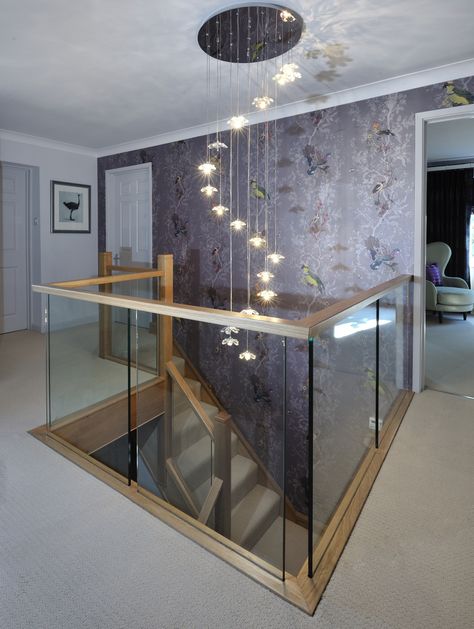 A centrally-positioned oak and glass staircase with a half-landing turn and gallery landing. Stunning chandelier lighting.