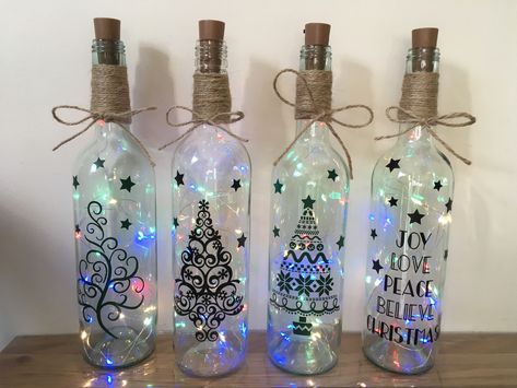 Light up wine bottles with Christmas themes Glass Bottles Christmas Decor, Wine Bottle Crafts Christmas Lights, Painted Light Up Bottles, Wine Bottle Cricut Projects, Cricut Glass Bottle Ideas, Light Up Wine Bottles Christmas, Painted Wine Bottles Christmas Ideas, Christmas Wine Bottle Lights, Christmas Glass Bottles Art