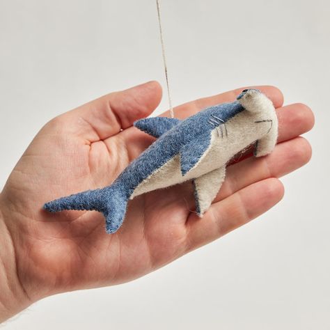 With his eyes mounted on the side of his head – our shark has 360-degree vision and can see above and below at all times! But don’t be scared - our little felt hammerhead loves to play. This adorable ornament is bound to jump from your tree and play with the kiddos. All details and stitching are hand-embroidered. Our ornaments come ready to hang with a string attached. Made from sustainably harvested merino-blended wool. Fairly traded and made with love. H: 2"/5cm W: 3.25"/8cm L: 5.5/14cm. Like Shark Felt, Shark Ornament, Shark Stuffed Animal, Felt Fish, Balloon Kits, Felting Ideas, Handmade Plushies, Felt Ornament, Hammerhead Shark