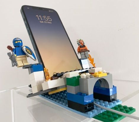 photo of a cell phone sitting in a holder made of legos and customized with characters and arch and flames Lego Desk, Diy Phone Stand, Diy Lego, Diy Space, Lego Characters, Cell Phone Stand, Desktop Accessories, Mobile Phone Holder, Phone Stand