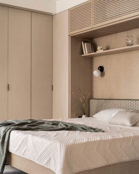 This guest bedroom exudes calm with light-toned finishes, featuring dyed oak wood veneer and beige textured laminate on wardrobes for added depth. The bed is designed to float above the floor, creating openness and maximizing space, while built-in shelves offer extra storage. Perforated shutters neatly conceal the AC unit, keeping the design sleek. A subtle green headboard adds a touch of color, complemented by custom bedside lights and built-in side tables. The paneled TV wall transitions in... Bed With Side Wardrobe, Wardrobe Above Bed, Paneled Tv Wall, Bed With Wardrobes Either Side, Hidden Vanity, Built In Bedroom, Bedside Wardrobe, Tiered Ceiling, Wardrobe Tv