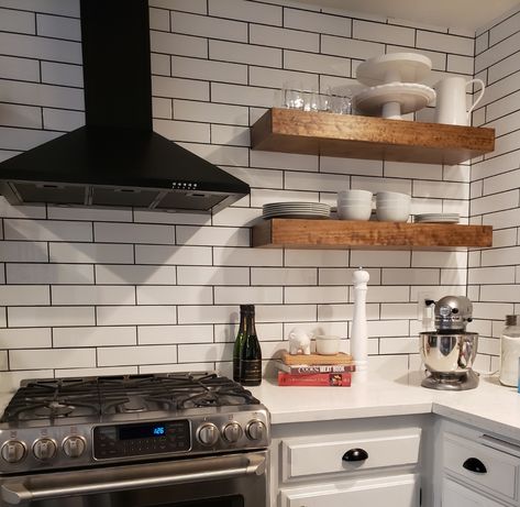 White subway tile with black grout, matte black oven hood and hand made floating shelves #beachhouse #beachremodel #homedecorideas Kitchen White Tile Black Grout, Black Oven White Kitchen, White Subway Tile Kitchen Backsplash With Floating Shelves, Kitchen Black Grout, White Tiles Black Grout Kitchen, White Subway Tile Black Grout Kitchen, Black Oven Hood, White Tile Black Grout Kitchen, White Backsplash With Black Grout