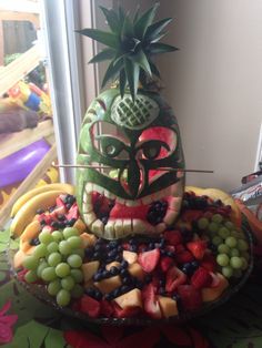 Carved watermelon tiki man Fruit For Luau Party, Tiki Watermelon Carving, Creepy Tiki Party, Tiki Food Ideas, Carved Watermelon Ideas, Tiki Party Food, Tiki Party Ideas, Watermelon Carving Ideas, Tiki Food