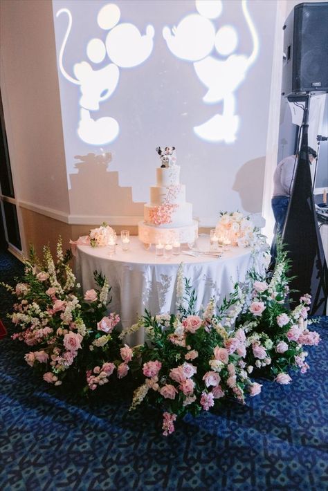 Disney Wedding cake table featuring Mickey and Minnie gobos, a white wedding cake with blush floral. Wedding Ceremony Inside, Romantic Disney, Hotel Disney, Cherry Blossom Wedding Theme, Wedding Table Themes, Disneyland Wedding, Disney Wedding Cake, Harry Potter Wedding Theme, Disney Weddings