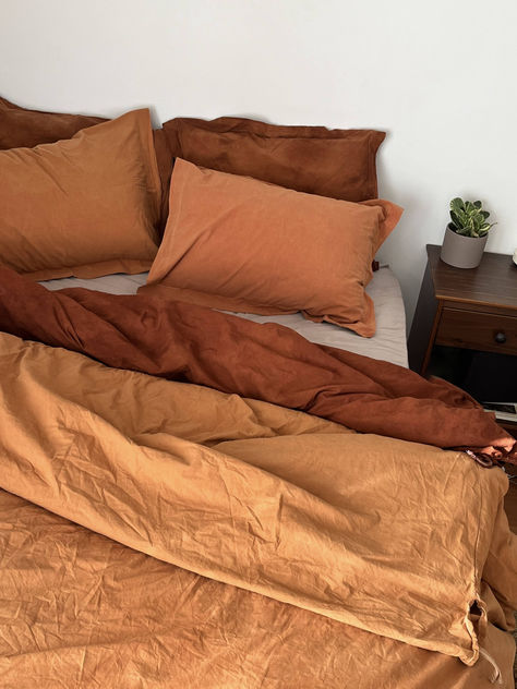 A bed with a terracotta colored duvet set and a tie dyed rust duvet set Sage Terracotta Bedding, Terracotta Yellow Bedroom, Orange Sheets Aesthetic, Mustard And Terracotta Bedroom, Bedding Color Combo Ideas, Bedroom Ideas Terracotta, Green Bedroom Paint Colors, Bedroom Aesthetic Green, Terracotta And Green Bedroom