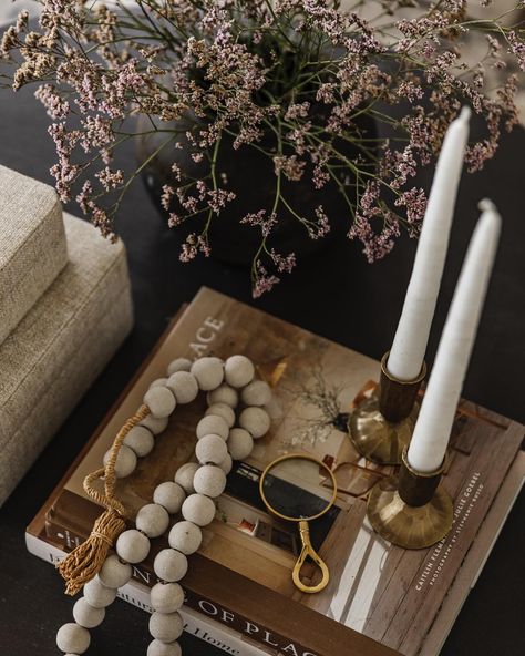 A few views of the same coffee table!! I love styling a coffee table. And on a round coffee table, I typically create a triangle. If you swipe over a few photos, you can see the vase of dried flowers creates the top of the triangle and then the stacked boxes and the stacked books create the left and right sides of the triangle. On the coffee table books we layered candle sticks for height and a cutie little magnifying glass and some beads for texture. 🖤 PC @katebohannan.studio Design & Styl... Coffee Table Candle Tray, Coffee Table Plant And Crystal Display, Stack Of Coffee Table Books, Wood Bead Garland Coffee Table, Coffee Table Styling Rattan Tray, Styling A Coffee Table, Layered Candles, Stacked Books, Candle Sticks