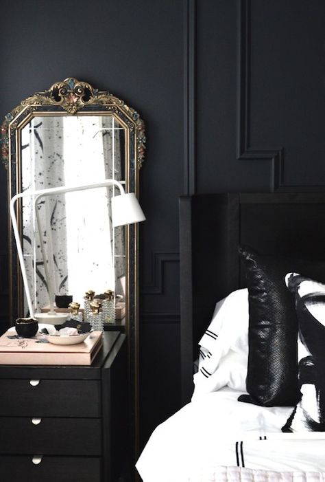 White and black bedroom features black walls adorned with black trim moldings framing a black wingback headboard on queen bed dressed in black and white hotel bedding as well as black and white pillows, Modern Circles Pillows, beside a black nightstand topped with an Ikea TISDAG LED Work Lamp in front of an antique mirror. Ikea Black Bedroom, Mirrors Behind Nightstand, White And Black Bedroom Ideas, Gustavian Bedroom, Christine Dovey, Bedside Styling, White And Black Bedroom, Ikea Aesthetic, Nightstands Ideas