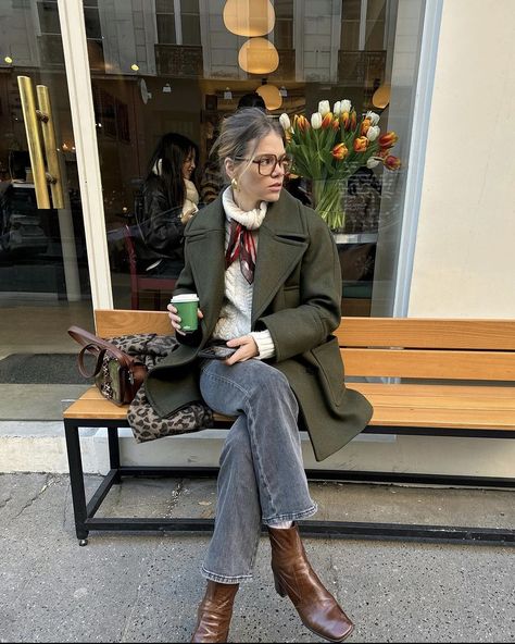 Parisian blond girl sitting on a bench with her coffee in hand. She is very in trend dressed. Her hair is up and is wearing brown squared glasses. She is wearing a thick white knitted turtleneck which she tied a thin elegant red satin  scarf around her neck. She associated this with grey jeans, brown leather block heels boots and a green jacket. Parisian Chic Style Fall, Paris Winter Fashion, Green Jacket Outfit, Fall Jackets Outfit, Outwear Outfit, Winter Outfits Ideas, Cardamom Buns, Khaki Coat, Christmas Instagram