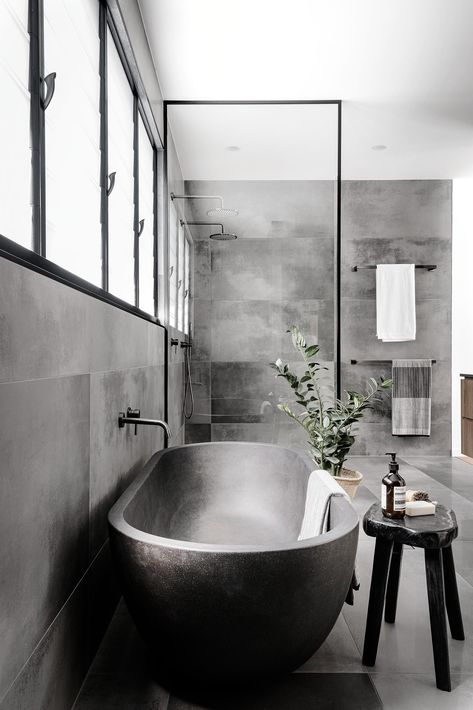 A modern master bathroom with large format grey tiles, a grey freestanding bathtub, and a black framed glass shower screen. Industrial Bathroom With Bathtub, Bathroom Black Bathtub, Grey Bathtub Ideas, Grey Industrial Bathroom, Black Bathtub Bathroom Ideas, Black Bathtub Bathroom, Bathtub Concrete, Open Bathtub, Grey Bathtub