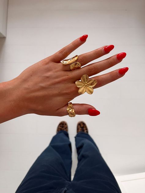 A close-up of a hand with red nail polish, wearing multiple gold rings including a flower ring, against a background of pants and leopard print shoes Summer Jewelry Stack, Chunky Ring Stack, Chunky Gold Jewelry, Chunky Jewelry, Dope Jewelry, Jewelry Lookbook, Stacked Jewelry, Jewelry Photography, Girly Jewelry