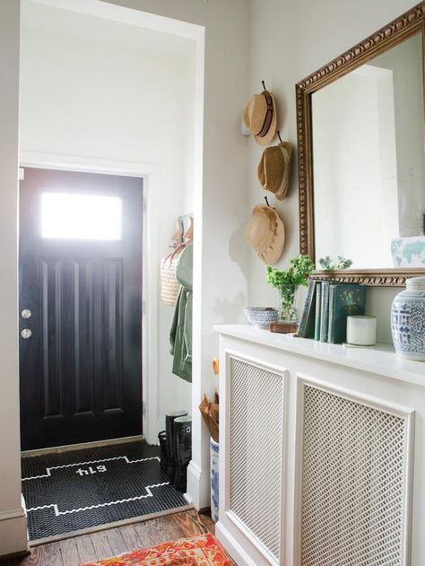 A vintage gold mirror hangs above an entry table created from the custom radiator cover in this eclectic home’s entryway. Pops of color are added with the vibrant antique rug and accessories while the black door and custom black and white tile work add sophistication to the space. Wall Heater Cover, Eclectic Entryway, Contemporary Radiators, Hallway Ideas Diy, Vintage Gold Mirror, Heater Cover, Entryway Mirror, Hallway Designs, Entry Hallway