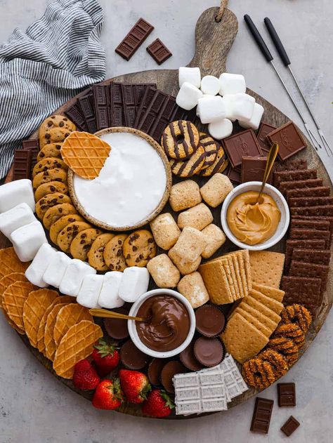 Just in time for summer barbecues and camping trips, this s'mores charcuterie board is here to sweeten things up! It features a mix of different types of chocolate, crackers, marshmallows, and spreads so everyone in your family can create their own perfect sweet treat. Camp Theme Charcuterie Board, S’more’s Charcuterie Board, Smores Dessert Board, S'more Platter, Halloween S’more Charcuterie Board, S’mores Ornament Diy, S’mores Charcuterie Boards, Bonfire Charcuterie Board, Smore Charcuterie Board Ideas