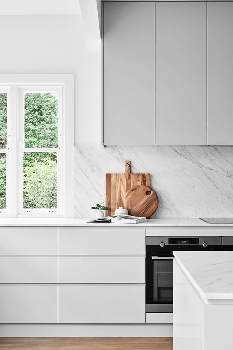 Gray Cabinets with White Backsplash and Sleek Appliances This contemporary kitchen has a very calm look characterized by light gray cabinets and a white marble backsplash whose feathery striations bring in undulating forms. Kitchen Interior Marble Top, Kitchen Carrara Marble, Kitchen Interior Grey And White, Soft Grey Kitchen Cabinets, Light Grey And White Kitchen, Kitchen Bench Styling, Soft Grey Kitchen, Kitchen Light Grey, Marble Top Kitchen