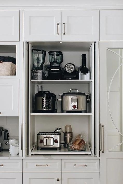 Fitted with pull out shelves, a small appliances cabinet is finished with white doors and nickel hardware and fixed beneath a white over head cabinet. Kitchen Appliances Cabinet, Cabinet With Pull Out Shelves, Appliances Cabinet, White Kitchen Shelves, Gorgeous White Kitchen, Kitchen Appliance Storage, Appliance Cabinet, Pull Out Shelves, Appliances Storage