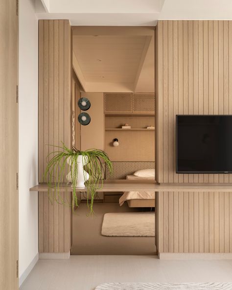 This guest bedroom exudes calm with light-toned finishes, featuring dyed oak wood veneer and beige textured laminate on wardrobes for added depth. The bed is designed to float above the floor, creating openness and maximizing space, while built-in shelves offer extra storage. Perforated shutters neatly conceal the AC unit, keeping the design sleek. A subtle green headboard adds a touch of color, complemented by custom bedside lights and built-in side tables. The paneled TV wall transitions in... Paneled Tv Wall, Wardrobe Headboard, Hidden Vanity, Wardrobe With Tv Unit, Minimalism Interior Design, Vanity In Bedroom, Tiered Ceiling, Tv Feature Wall, Sons Room