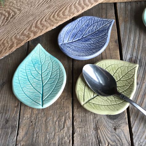 "Set of 3 leaf ring dishes, spoon rests, rustic leaf bowls, leaf ring bowls - Each handmade Earthenware ceramic bowl is impressed with an actual leaves. Perfect for a farmhouse kitchen.   Bowls were slump molded on smooth beach stones to give them shape.   Perfect for holding tea bags, spoons, rings or pills.  One of each color is included in the set of 3: Select Sage/navy blue/ turquoise OR Sage/green/turquoise sets of leaves.  Hand painted with underglaze and gloss glaze and kiln fired to prod Clay Spoon Rest Pottery, Pottery Spoon Rest Ideas, Spoon Rest Pottery Painting Ideas, Hydrangea Leaf, Ring Bowls, Leaf Pottery, Itsekovettuva Savi, Pottery Spoon Rest, Earthenware Ceramics