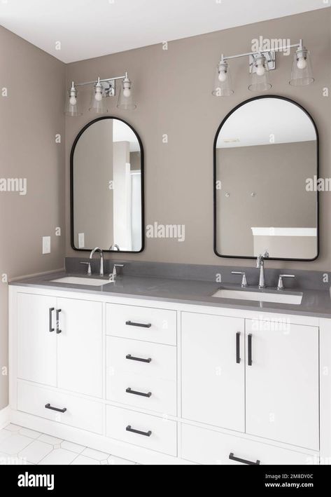 Download this stock image: A bathroom with a white vanity and black hardware, chrome faucets on a quartz countertop, arched mirrors, and brown walls. - 2M8DY0C from Alamy's library of millions of high resolution stock photos, illustrations and vectors. Quartz Bathroom Countertops, Arched Mirrors, Silver Faucet, Black Faucet, Finished Bathrooms, Gray Vanity, Chrome Faucet, Quartz Countertop, Arch Mirror